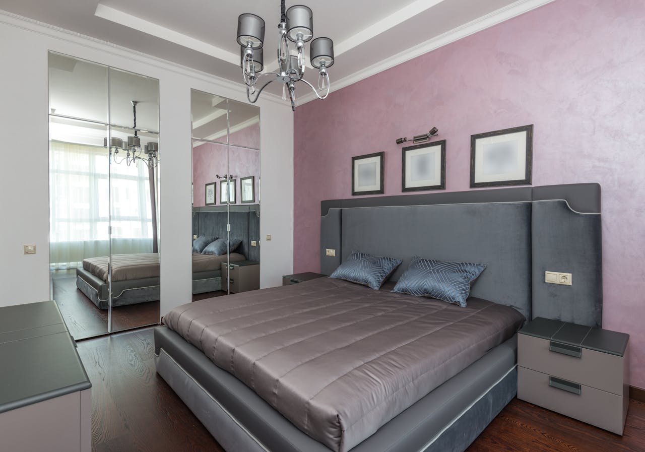 Stylish hotel bedroom featuring a luxurious bed, mirrored wardrobe, and lilac walls.